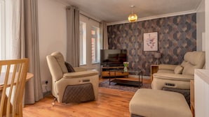 Una sala moderna con sofá, sillón, reposapiés, televisión y pared con estampado.