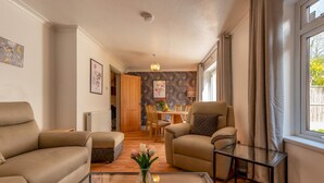 Una sala de estar con sofá, sillón y mesa de centro, un comedor con mesa y sillas, y vista al exterior a través de una ventana.