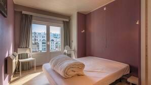 A hotel room with a bed, a chair, a desk, and a window with curtains. - Cosy Renovated Flat on the Seafront (Koksijde)