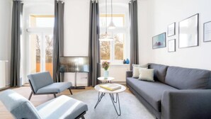A modern living room with a grey sofa, a grey armchair, a small round table, and a TV on a stand. - Bright & Stylish Apartment in Berlin's Sprengelkiez (Berlin)