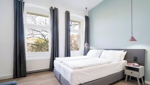 A modern bedroom with a bed, bedside table, and a window with curtains. - Bright & Stylish Apartment in Berlin's Sprengelkiez (Berlin)