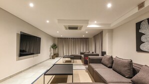 Ein modernes Wohnzimmer mit einem Ecksofa, einem Flachbildfernseher, einem Couchtisch und einer Topfpflanze.