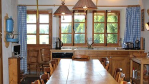 Une cuisine avec une longue table en bois, des chaises en bois, un évier et des lampes en cuivre suspendues au plafond.