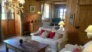 L’intérieur d’un chalet en bois chaleureux, avec une table en bois, un canapé blanc agrémenté de coussins à motifs floraux et un téléviseur en arrière-plan.