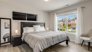 Ein modernes Schlafzimmer mit einem großen Bett, Nachttischen, einem Fenster mit Vorhängen und Blick auf Nachbarhäuser.