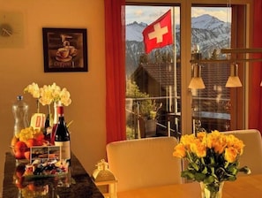 Un comedor con una mesa dispuesta para dos personas, una bandera suiza y vistas a la montaña.