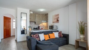 A modern living room with a grey sofa, a small wooden side table, and a potted plant. - Modern studio with ocean views and heated pool in Malibu Park (San Eugenio Alto)
