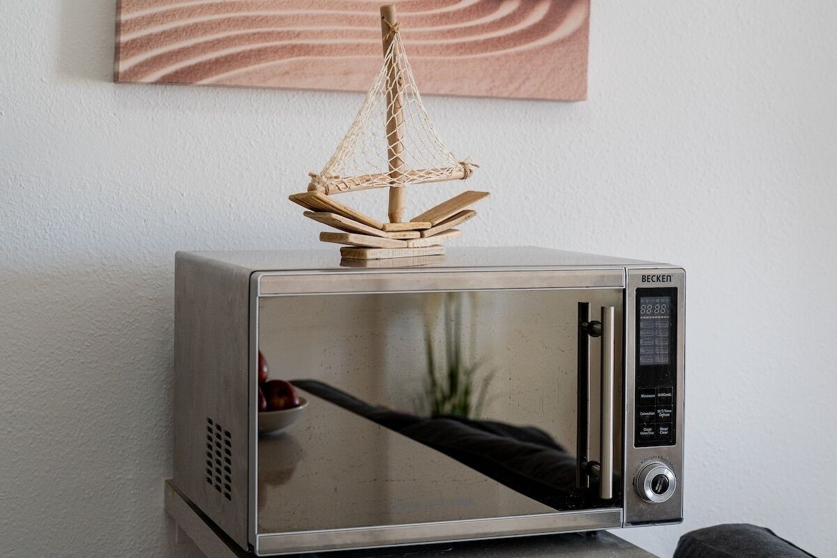 A microwave with a wooden sailboat model on top.