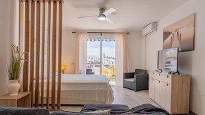 A hotel room with a bed, a desk, a TV, a balcony with a view, and a ceiling fan. - Modern studio with ocean views and heated pool in Malibu Park (San Eugenio Alto)