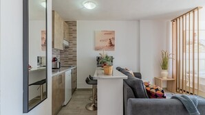 A modern kitchen with a central island, a dining area with a grey sofa, and a large window with a view. - Modern studio with ocean views and heated pool in Malibu Park (San Eugenio Alto)