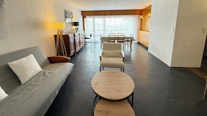 A modern living room with a sofa, a round wooden table, and a dining area with a table and chairs.