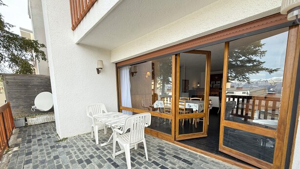 A patio with a table and chairs, a sliding glass door leading to an indoor dining area, and a satellite dish on the left.