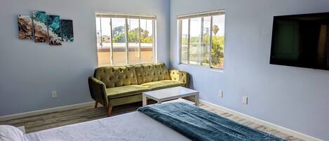 A room with a bed, a sofa, a small table, and two windows.