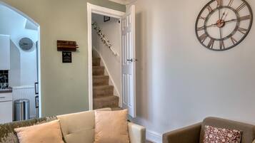 A living room with a sofa, a chair, a clock, and a staircase leading to a kitchen.
