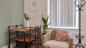 Een eetruimte met een houten tafel, zwarte stoelen, een witte vaas met bloemen, en een bordje met de tekst 'EAT well' aan de muur.