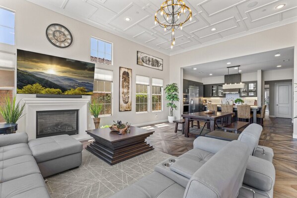 A spacious living room with a fireplace, a dining area, and a kitchen in the background.