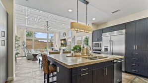 A modern kitchen with dark cabinetry, stainless steel appliances, and a large island with seating. - 2BR retreat - hot tub, gym & Coachella nearby (La Quinta)