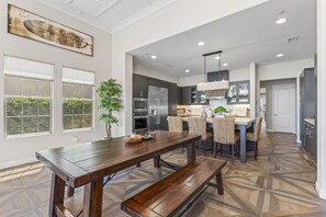 A modern kitchen with dark cabinetry, stainless steel appliances, and a wooden dining table with chairs.