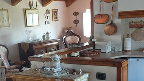 Ein gemütliches Wohnzimmer mit Holzbalkendecke, einem Korbuscheinmöbel, einem weißen Sofa und einer Küchenzeile mit Kupfergeschirr und einem Toaster.