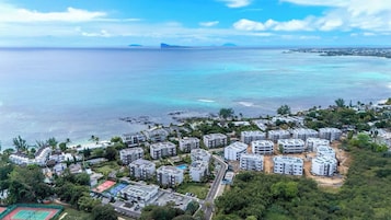 Un área residencial costera con varios edificios de apartamentos, vista despejada del océano y una isla distante.