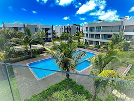 Un hotel moderno con una piscina central rodeada de palmeras y un cielo azul despejado.