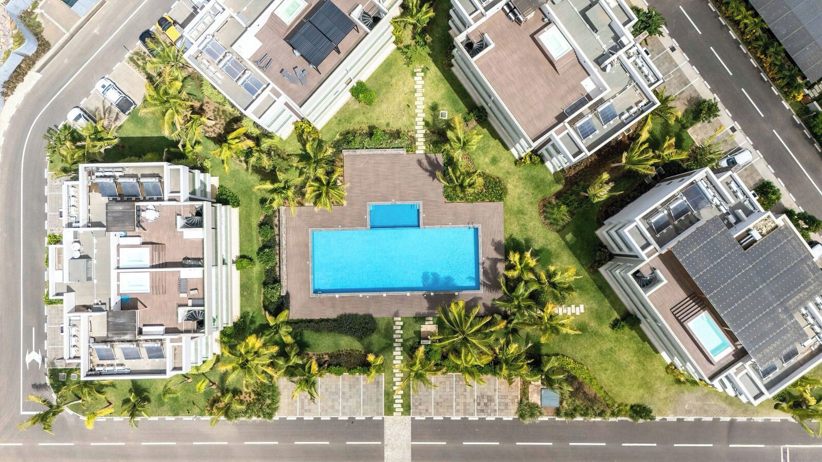 Vista aerea di un moderno resort con una piscina centrale, diverse ville per gli ospiti e una rigogliosa vegetazione.