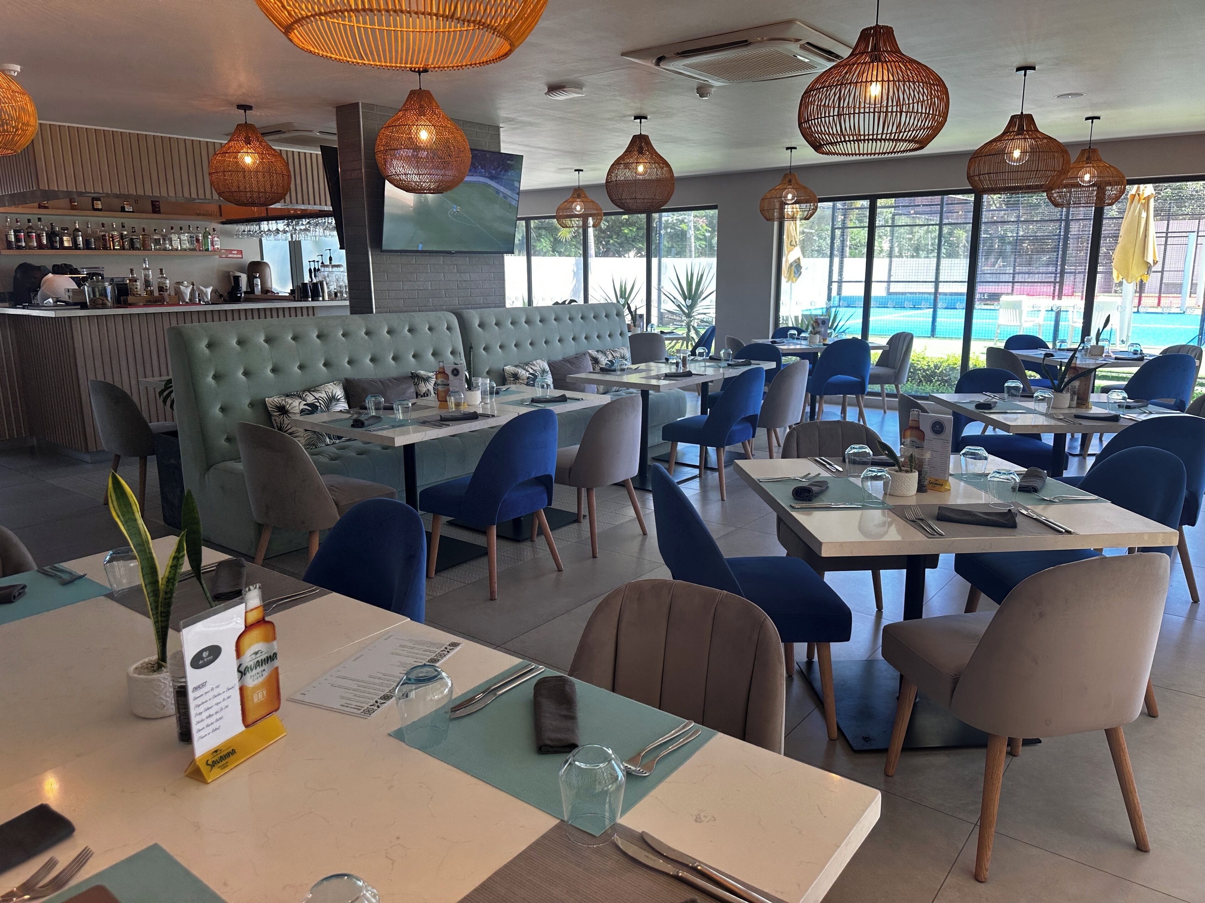 Un restaurante con zona de bar, mesas y sillas, y un amplio ventanal con vistas al exterior.