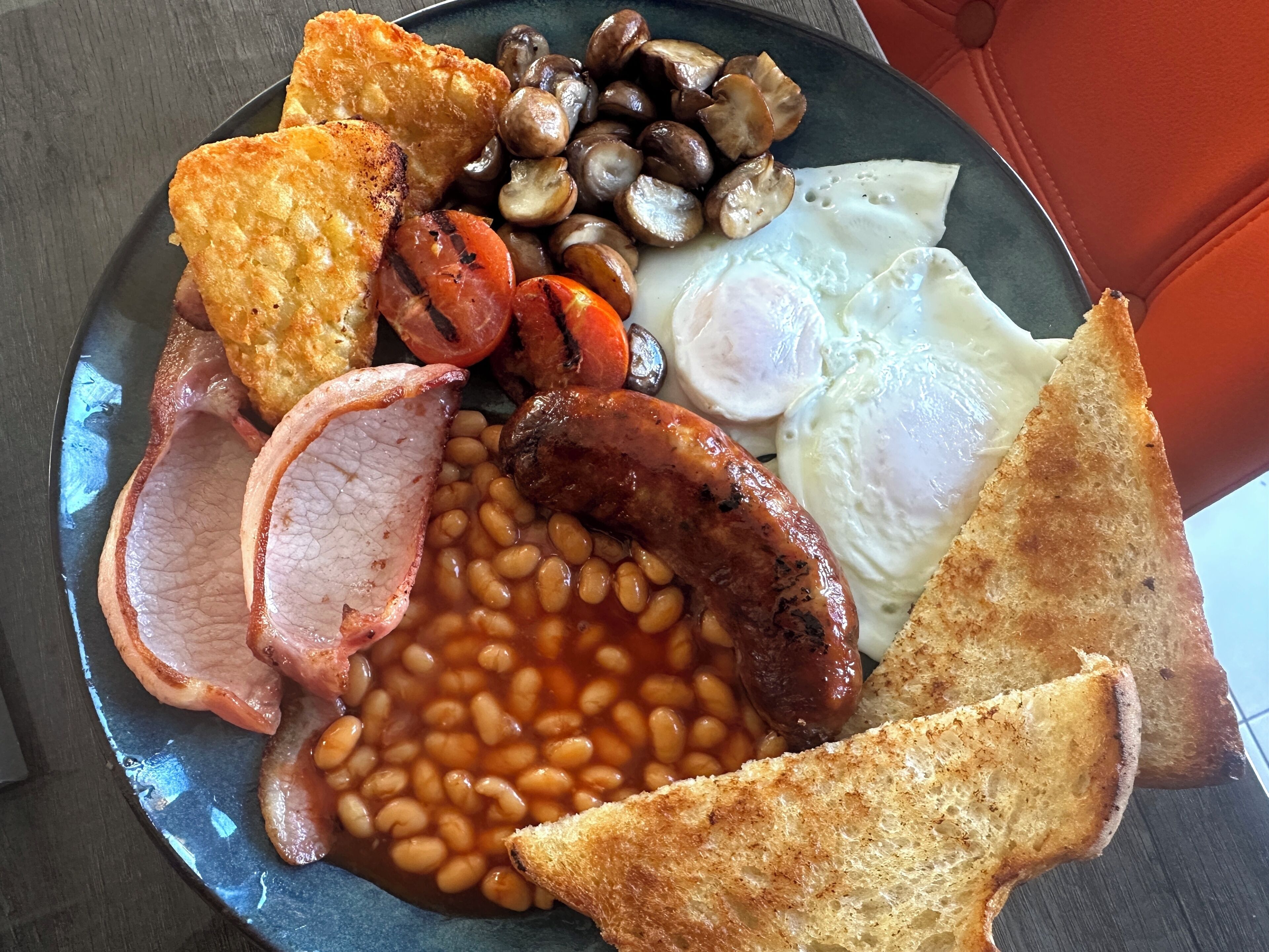 A plate of breakfast food including toast, eggs, sausages, beans, mushrooms, and bacon.