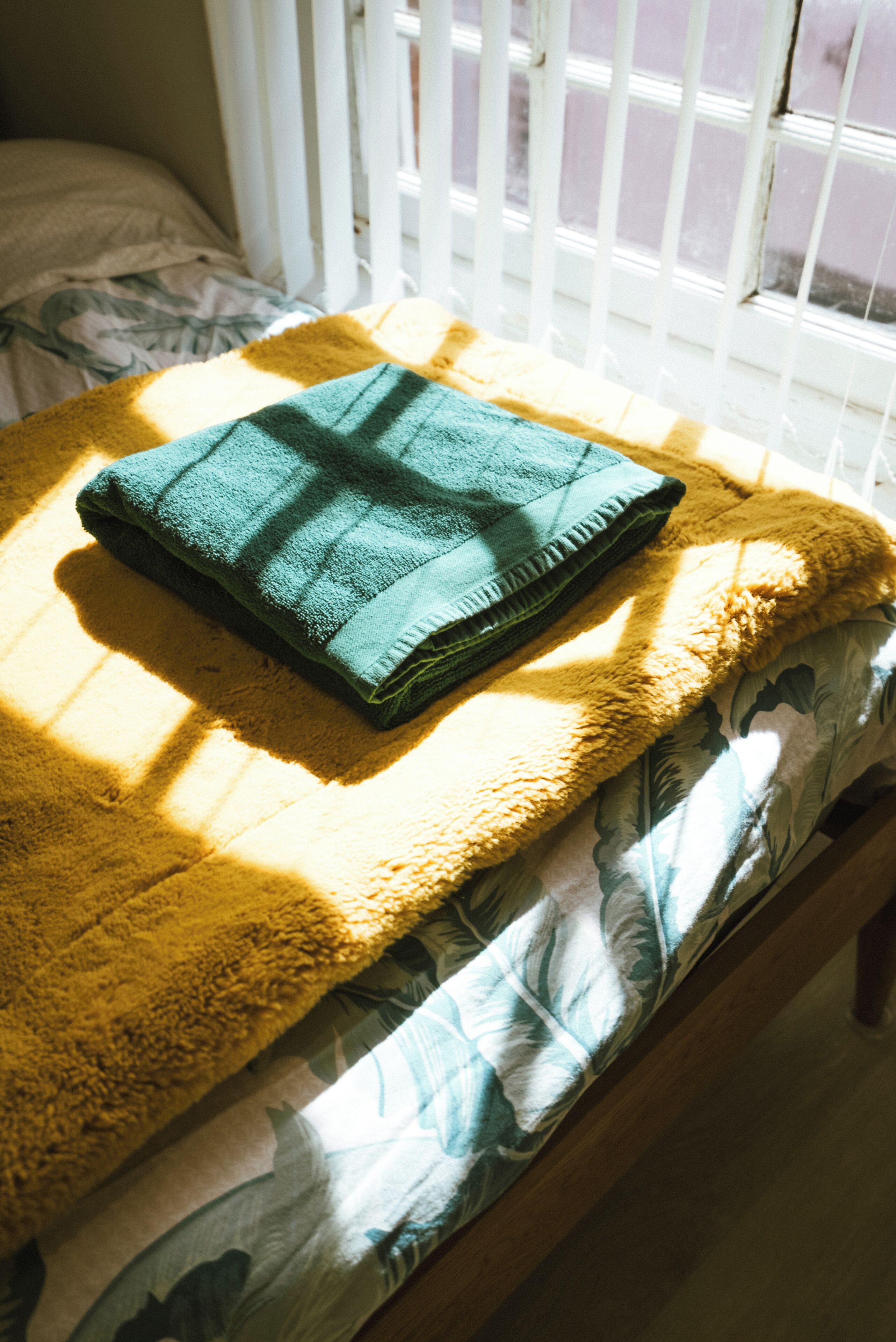 Een bed met een groen opgevouwen deken en een gele deken op een houten bedframe.