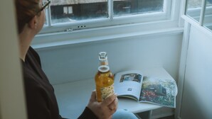 A person sitting by a window with a view of boats on the water, holding a bottle, and reading a magazine. - The Old Captains Lookout (Falmouth)