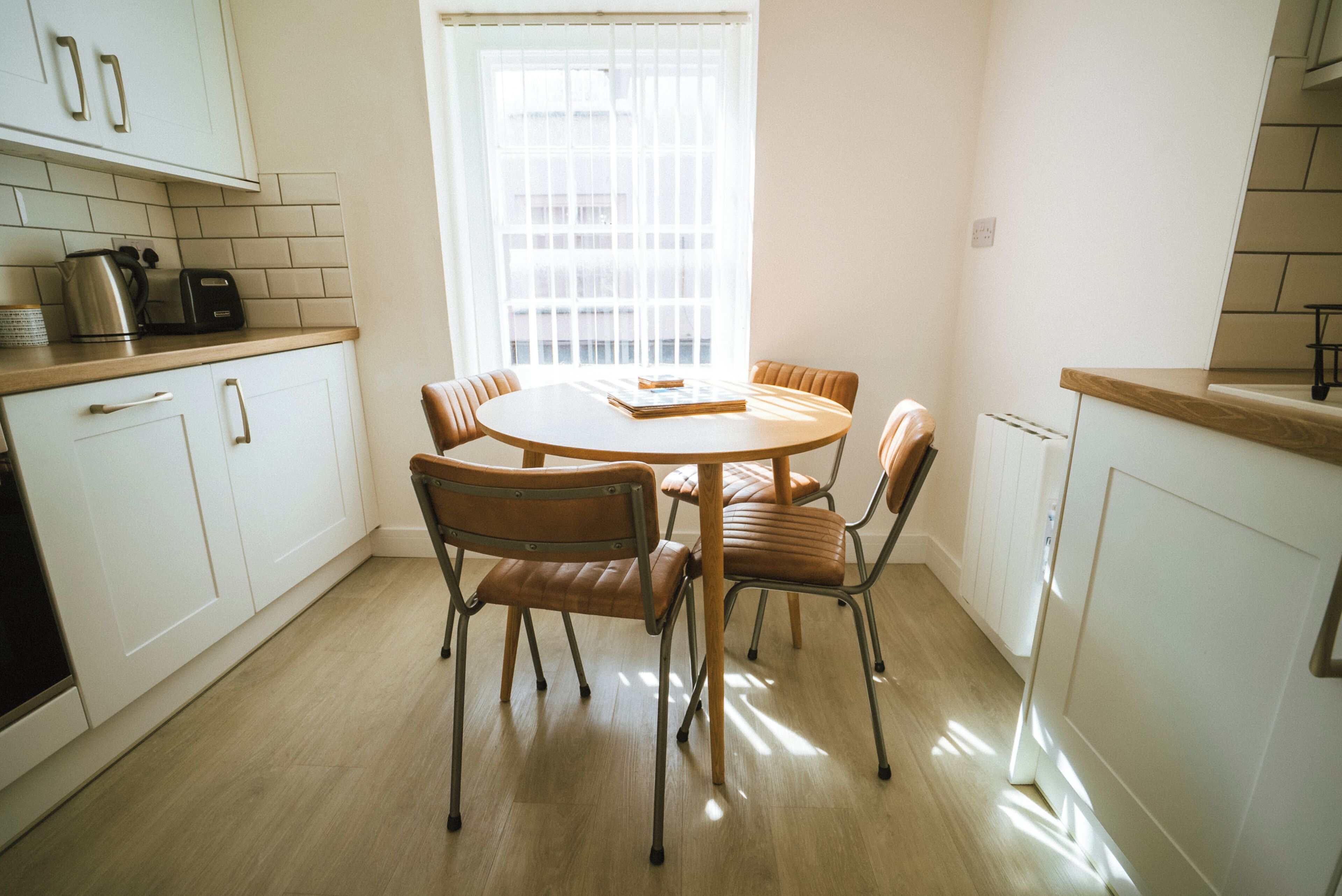 A modern kitchen with white cabinets, a round dining table, and six brown chairs.