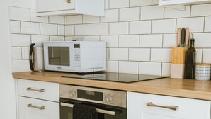 A kitchen with white cabinets, a microwave, a dishwasher, and a wooden table with chairs. - The Old Captains Lookout (Falmouth)