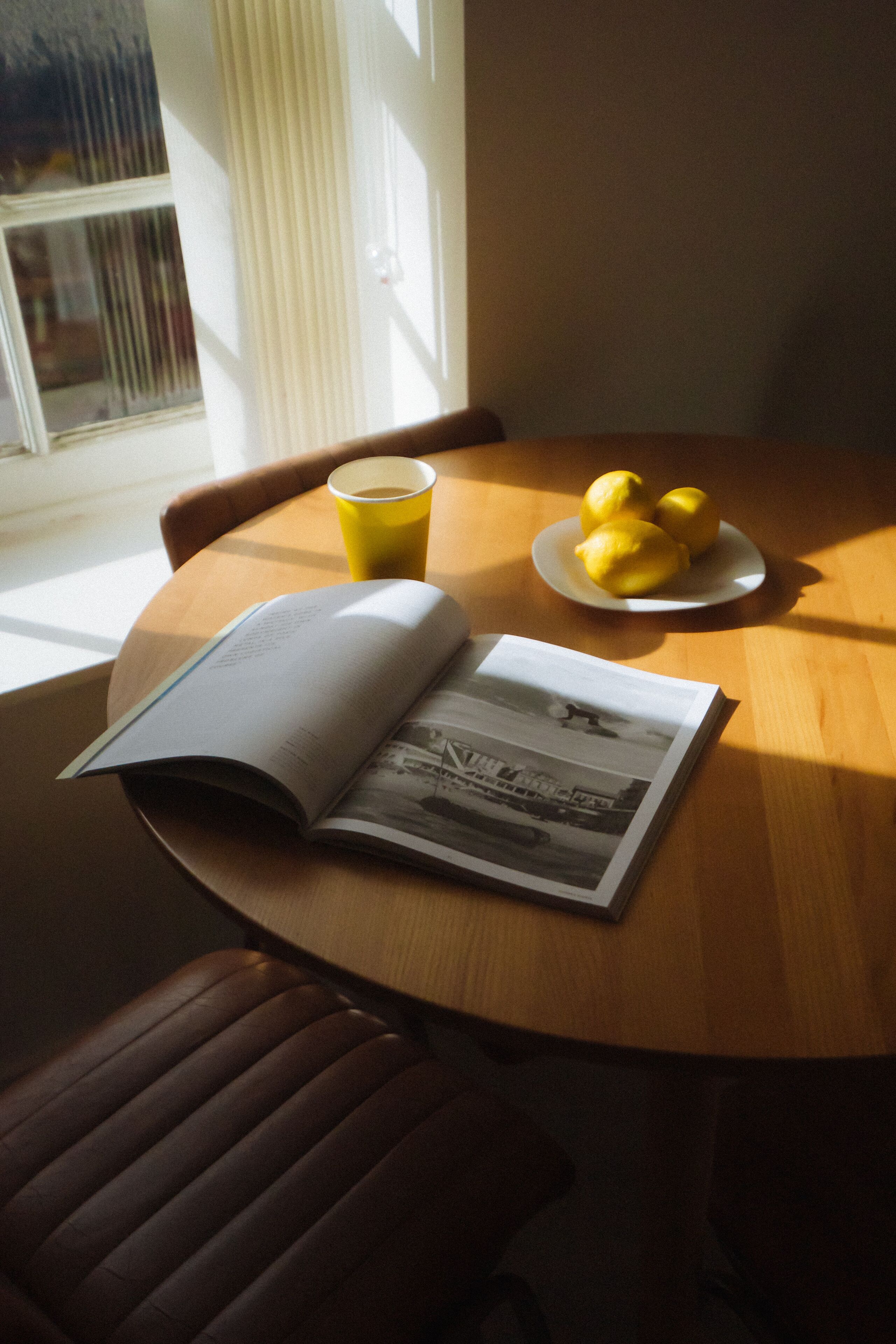 A table with a book, a plate of lemons, and a yellow cup.