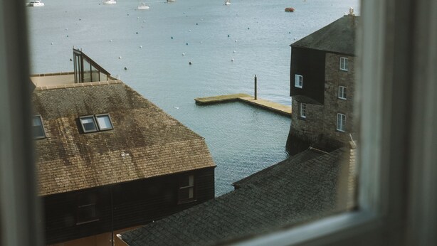 A coastal view from a window overlooking a harbor with boats, a dock, and buildings. - The Old Captains Lookout (Falmouth)