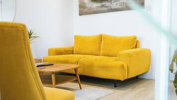A modern living room with a yellow sofa, a wooden coffee table, and a painting of a boat on the wall.