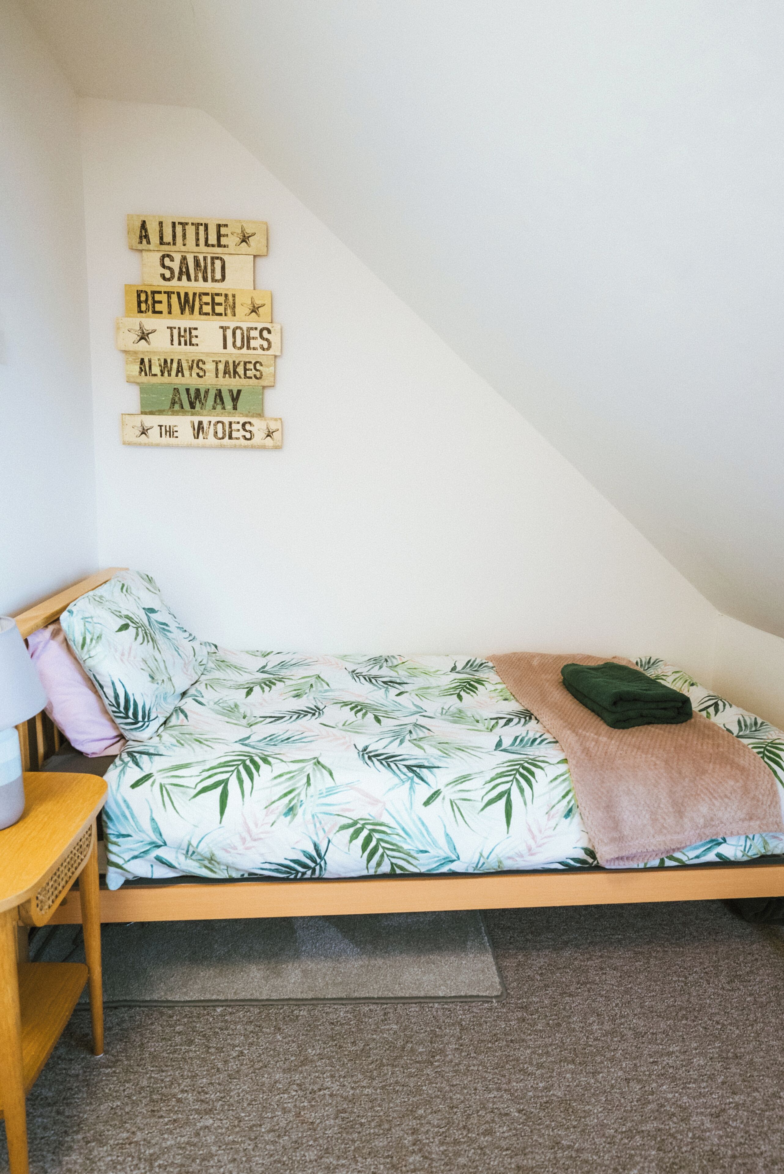 Ein Schlafzimmer mit Bett, Nachttisch, einem an der Wand befestigten Schild und Teppichboden.