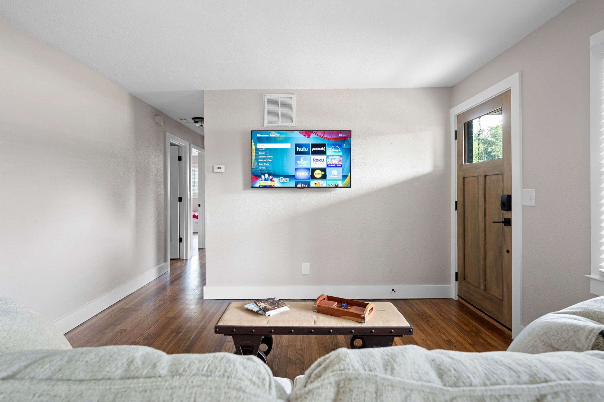 Sala de estar com televisão de tela plana fixada na parede, exibindo diversos serviços de streaming.