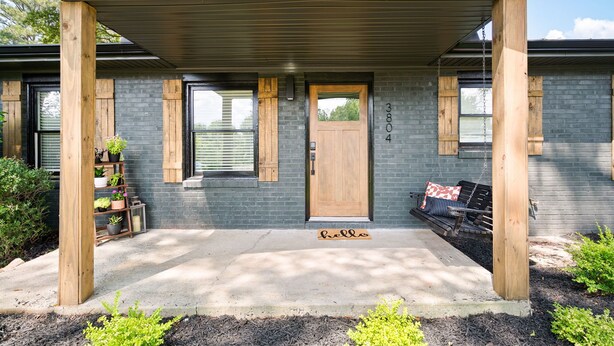 A modern house with a grey brick exterior, a wooden door, and a bench outside. - At Home in Acworth! (Acworth)