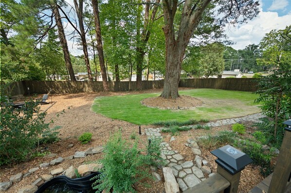 Un jardin avec un chemin de pierres, un grand arbre et une pelouse bien entretenue.