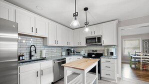 A modern kitchen with white cabinets, a stainless steel refrigerator, a microwave, and a wooden table. - At Home in Acworth! (Acworth)