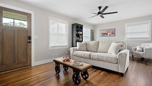 A living room with a wooden floor, a beige sofa, a coffee table, and a ceiling fan. - At Home in Acworth! (Acworth)