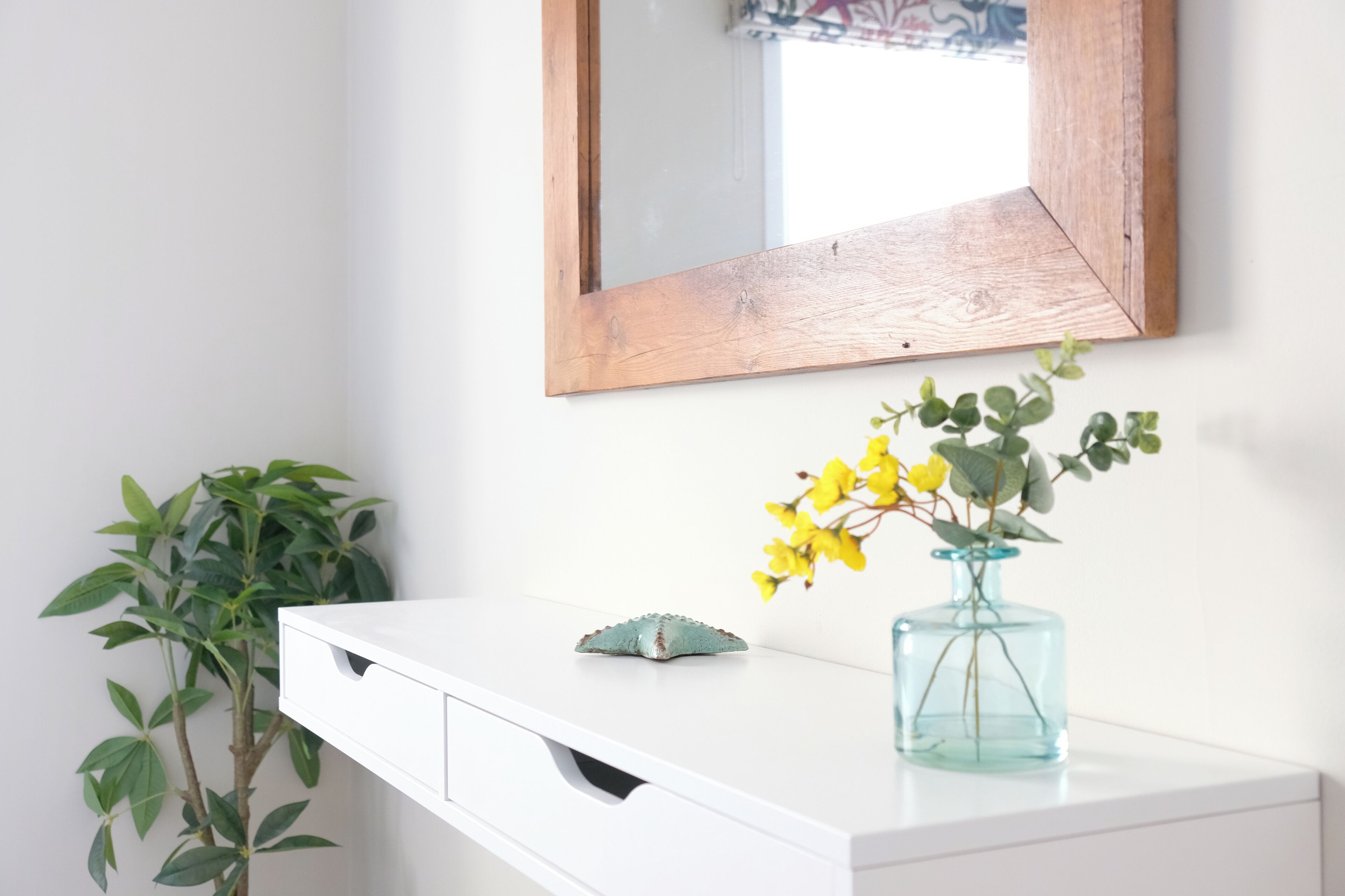 A white vanity with a mirror, a small decorative item, and a vase with yellow flowers.