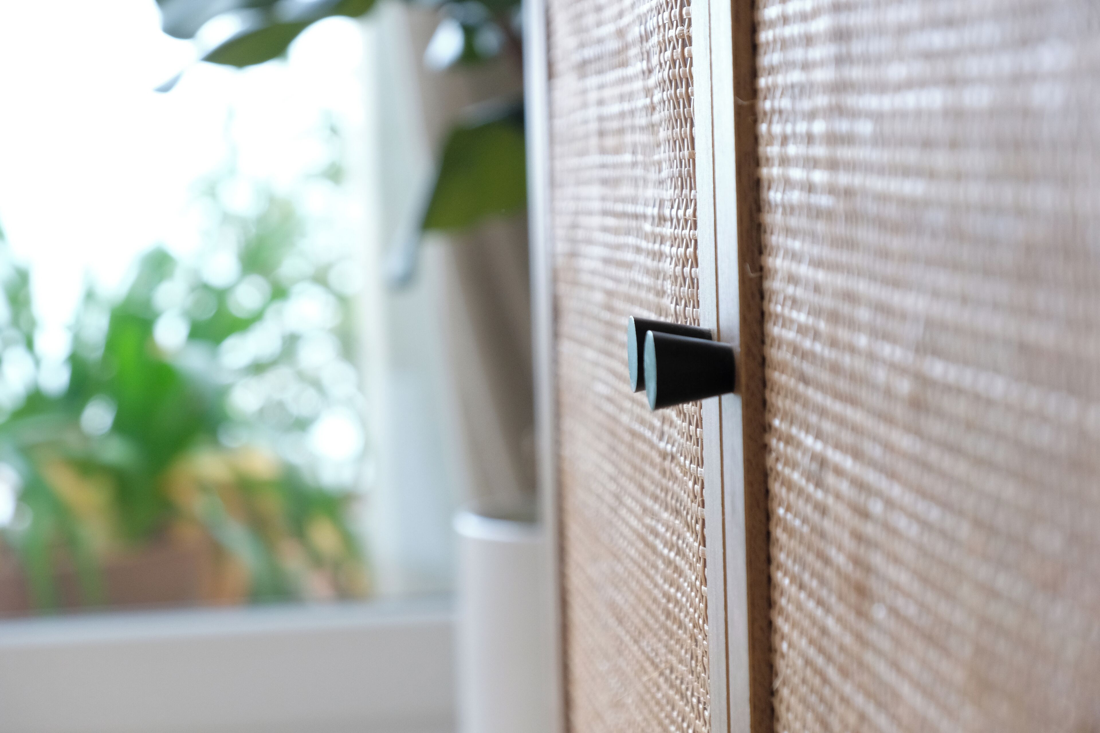 A close-up of a woven room divider with a black handle, suggesting a partition within a room.