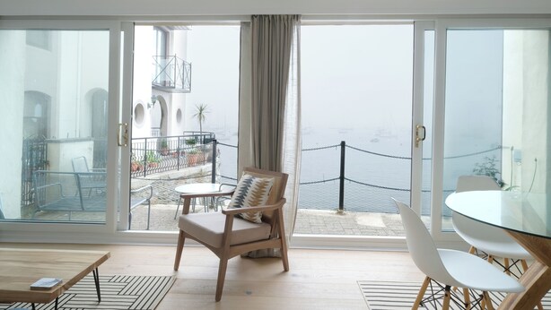 En balkon med havudsigt og både, med en stol, et bord og gelænder.
