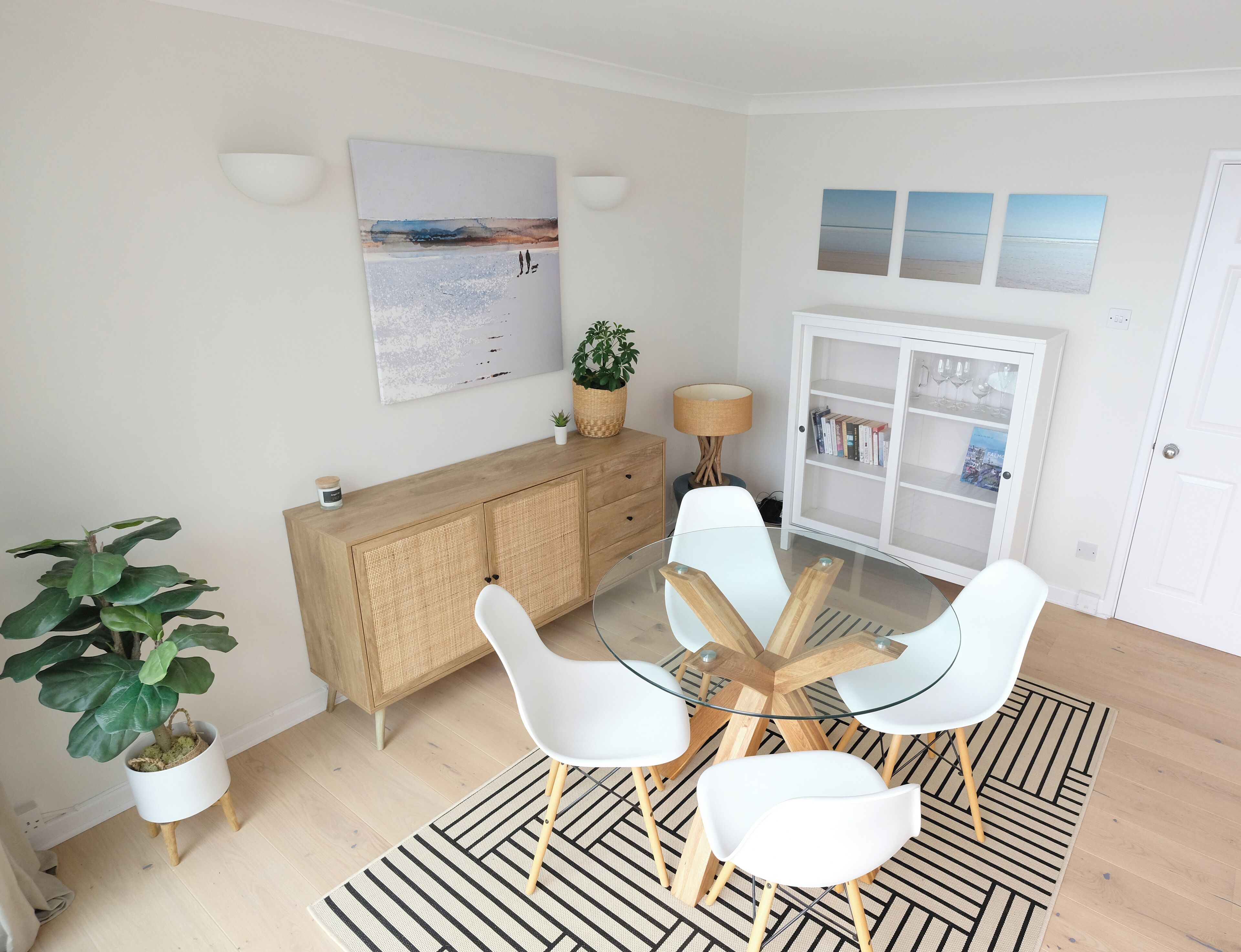 Un comedor moderno con una mesa de vidrio, sillas blancas, un mueble de madera y una planta grande en maceta.