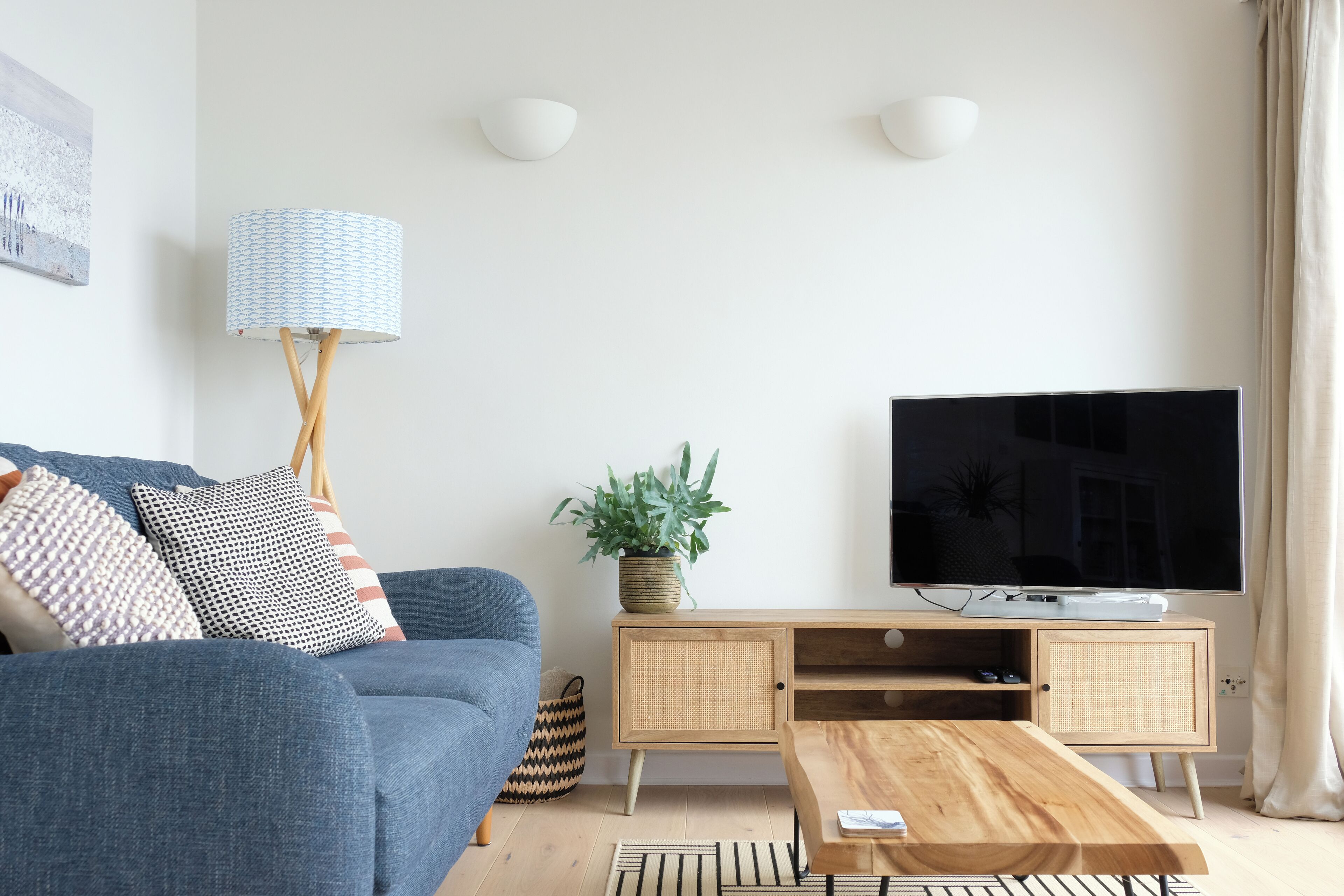 Un salon moderne avec un canapé bleu, une table basse en bois, un téléviseur à écran plat, une lampe et une plante.