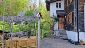 Una rustica casa in legno con una pergola in legno, una panchina in legno e una scalinata in pietra che conduce all'ingresso.