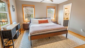 Un dormitorio con cama, mesitas de noche, un escritorio, un ventilador de techo y una ventana.