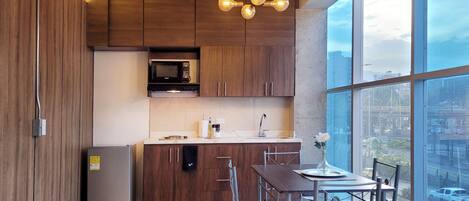 A modern kitchen with wooden cabinets, a stainless steel refrigerator, a microwave, and a dining area with a table and chairs.