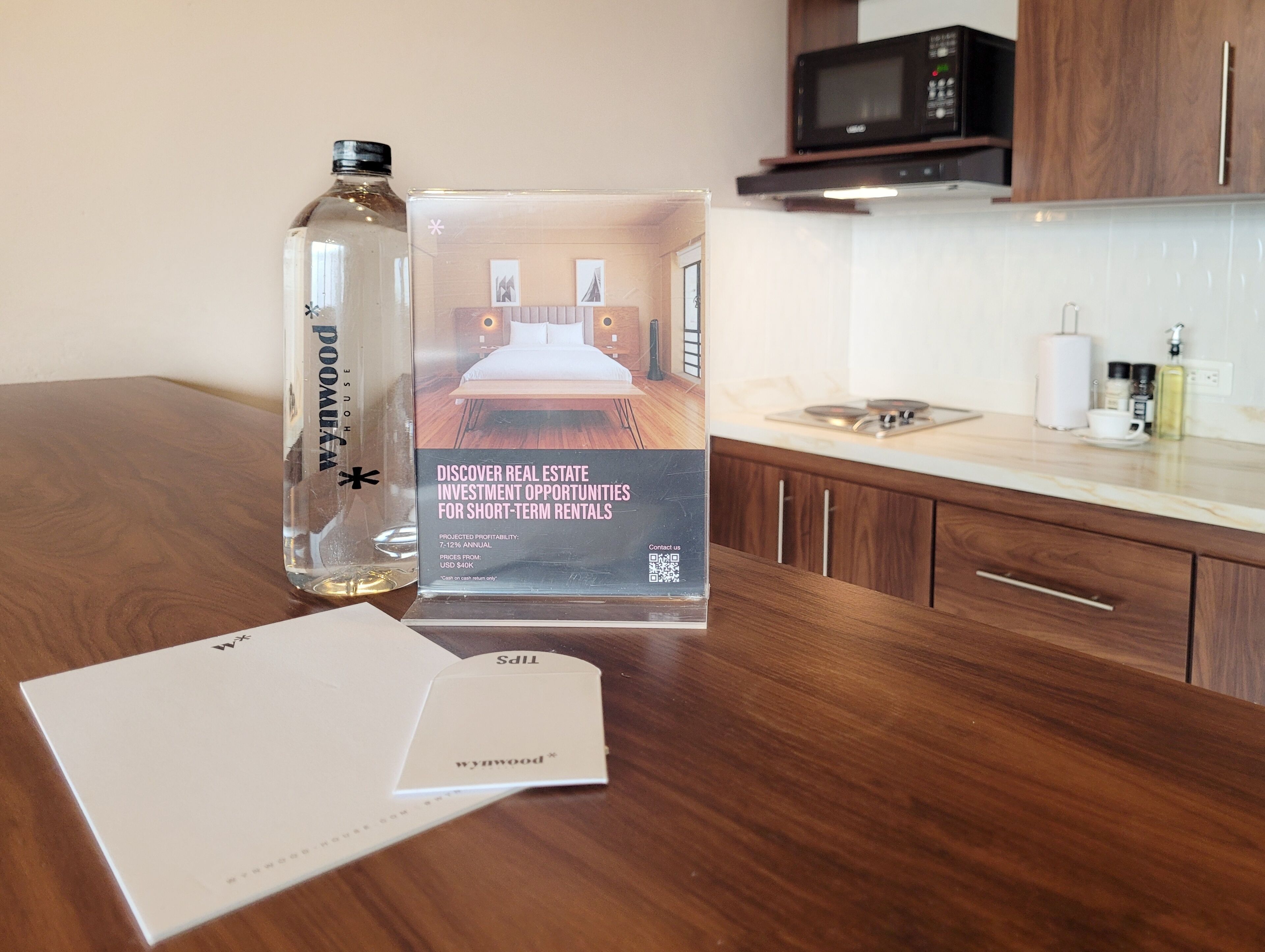 Une brochure présentant les opportunités d’investissement immobilier dans le domaine de la location de courte durée, une bouteille d’eau et un coin cuisine équipé d’un four à micro-ondes et de placards.